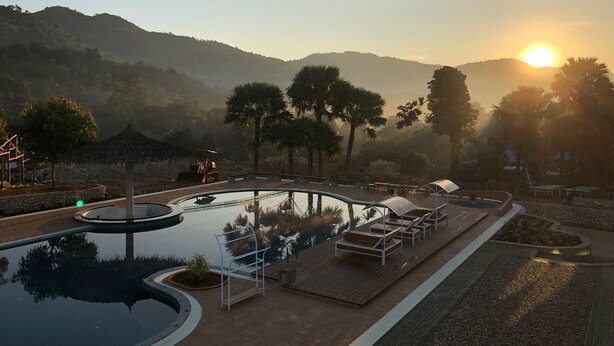 Zona de piscina con sillones de descanso, una piscina circular pequeña y vistas al atardecer sobre un paisaje montañoso.