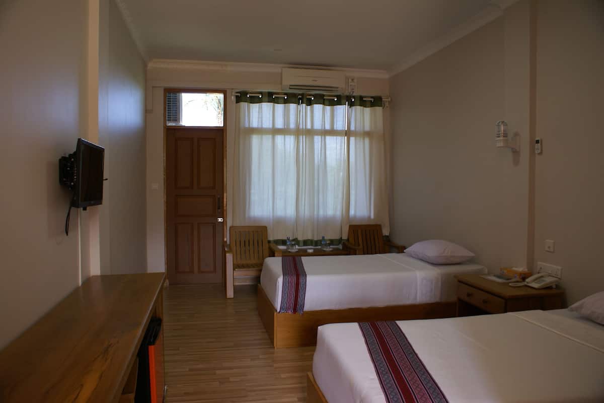 A hotel room with two beds, a wooden desk, a chair, a small table, and a TV mounted on the wall.