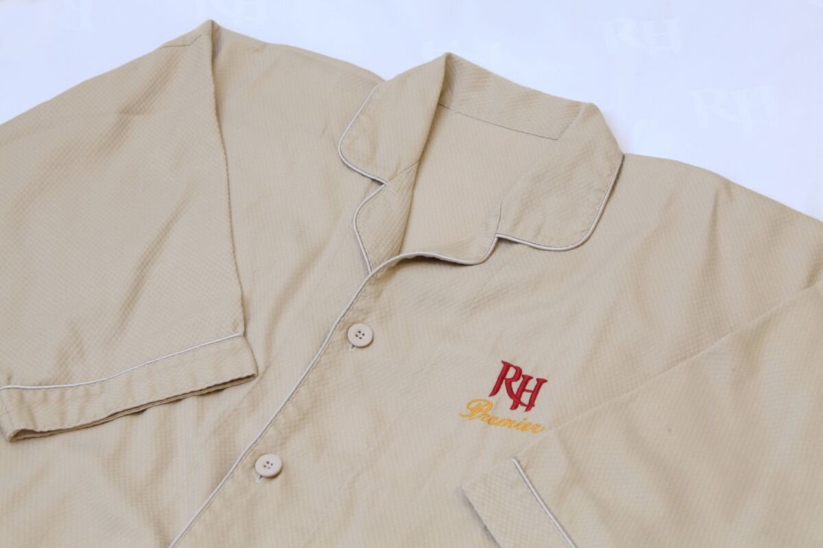 A beige shirt with a collar, buttons, and embroidered text.