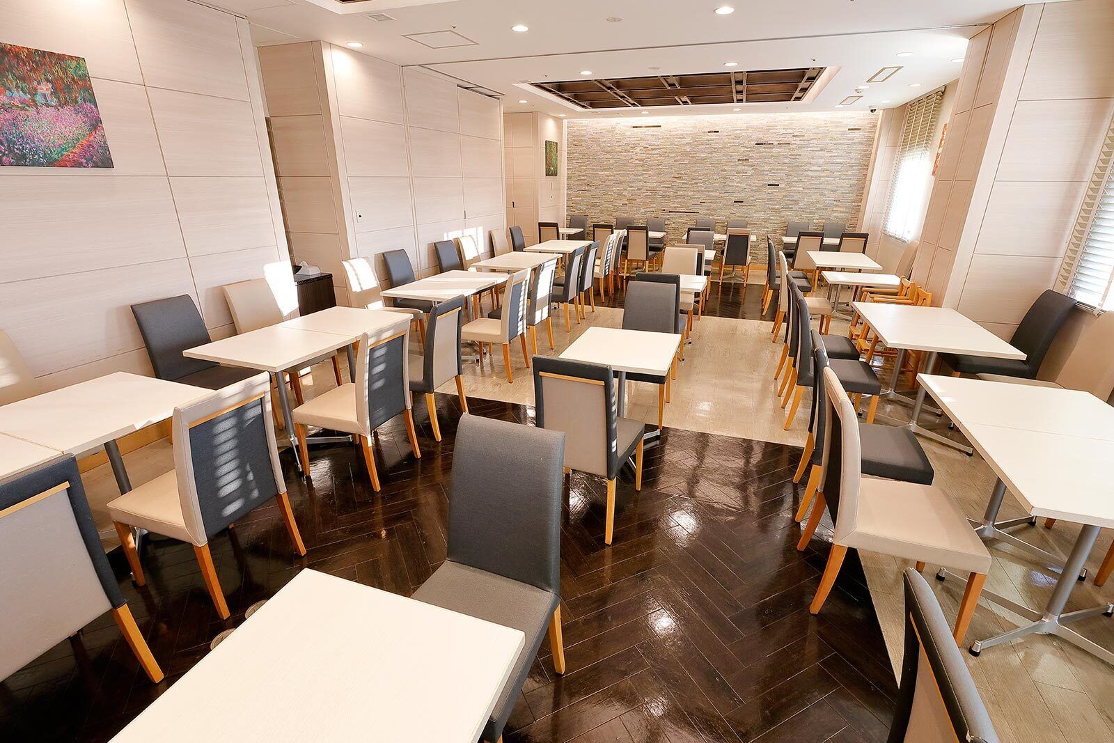 A conference room with multiple tables and chairs, a stone wall, and a painting on the wall.