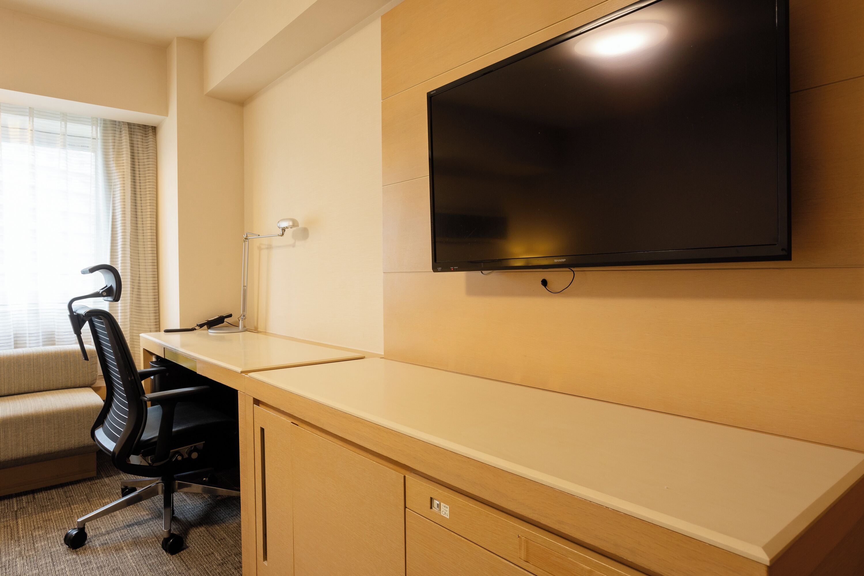 A hotel room with a desk, chair, television, and a window with curtains.