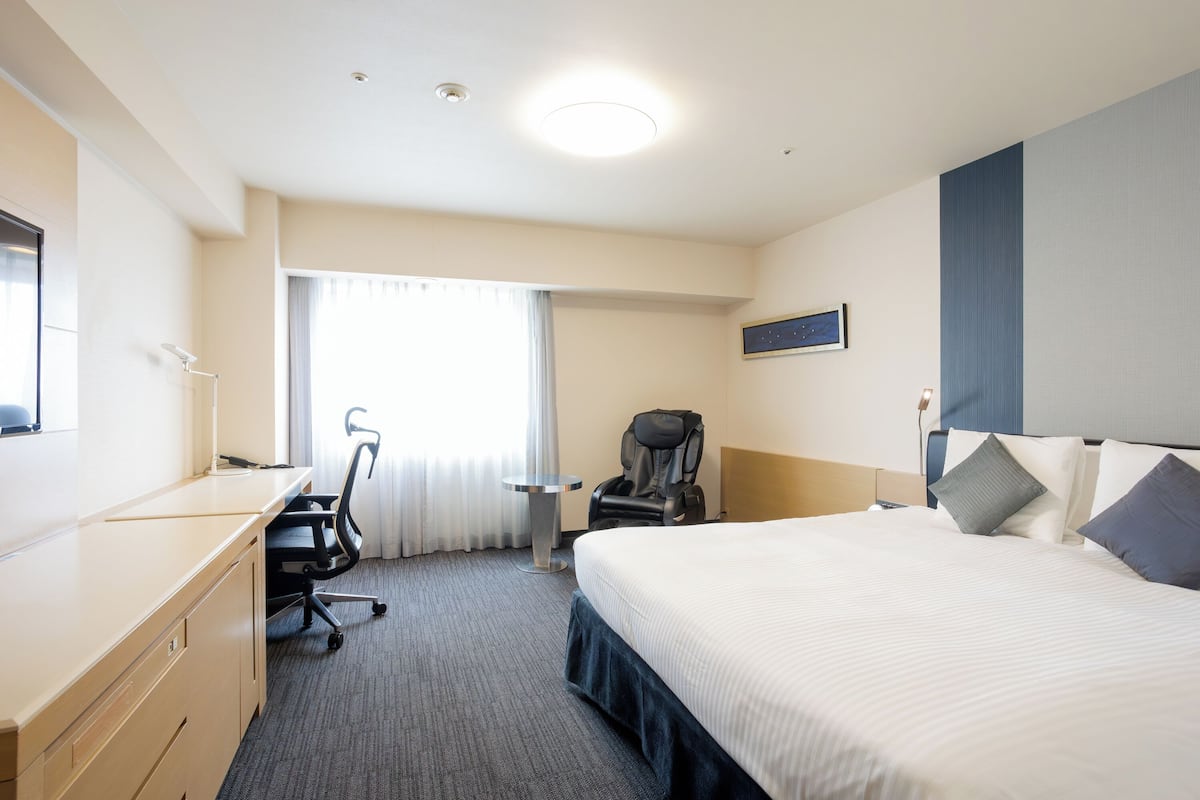 Een hotelkamer met een bed, bureau, stoel en een raam met gordijnen.