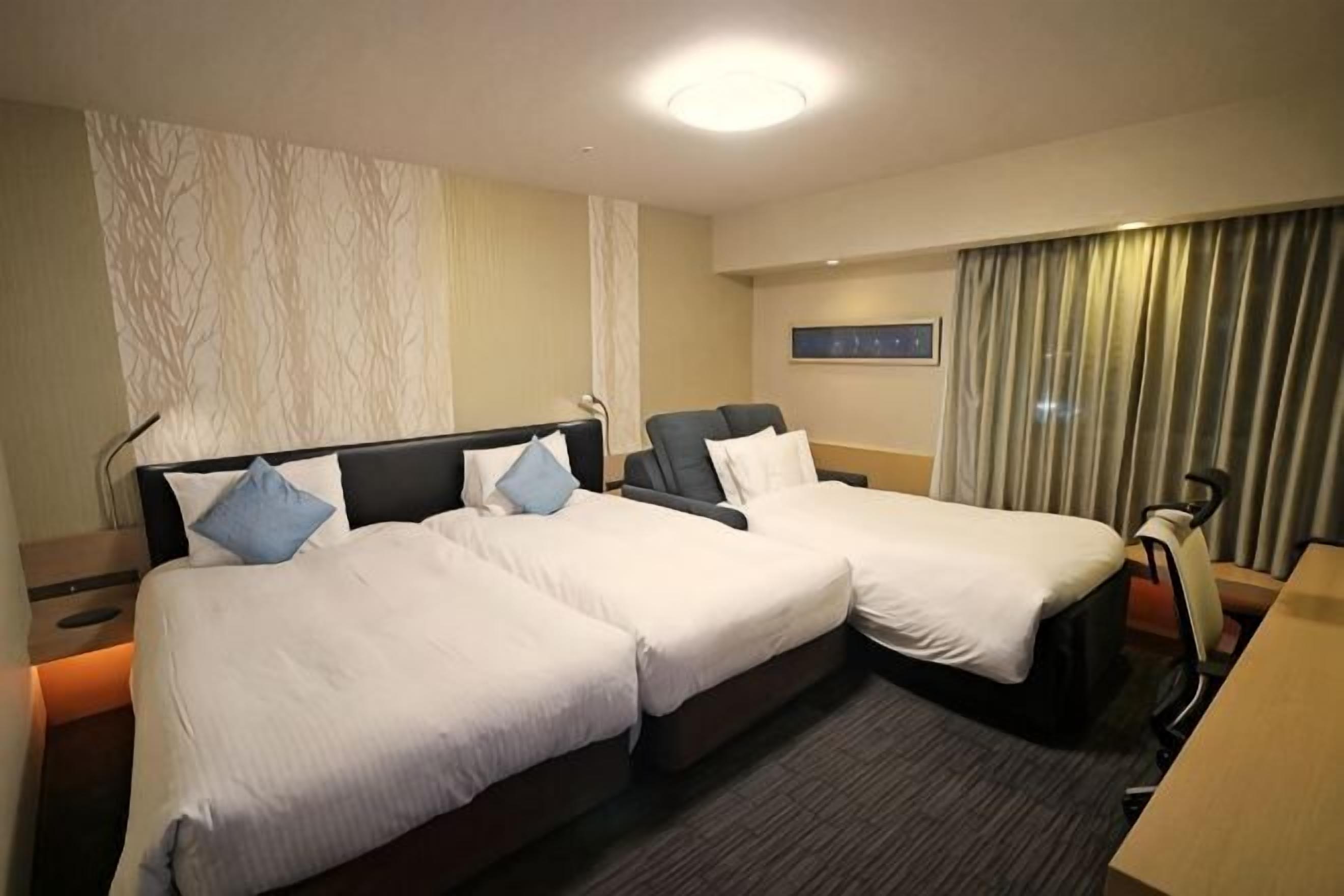 Une chambre d’hôtel avec deux lits, un bureau, une chaise et un rideau.