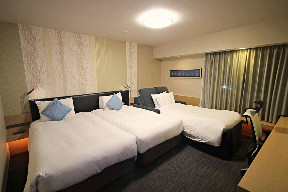 Een hotelkamer met twee bedden, een bureau, een stoel, een nachtkastje en een raam met gordijnen.