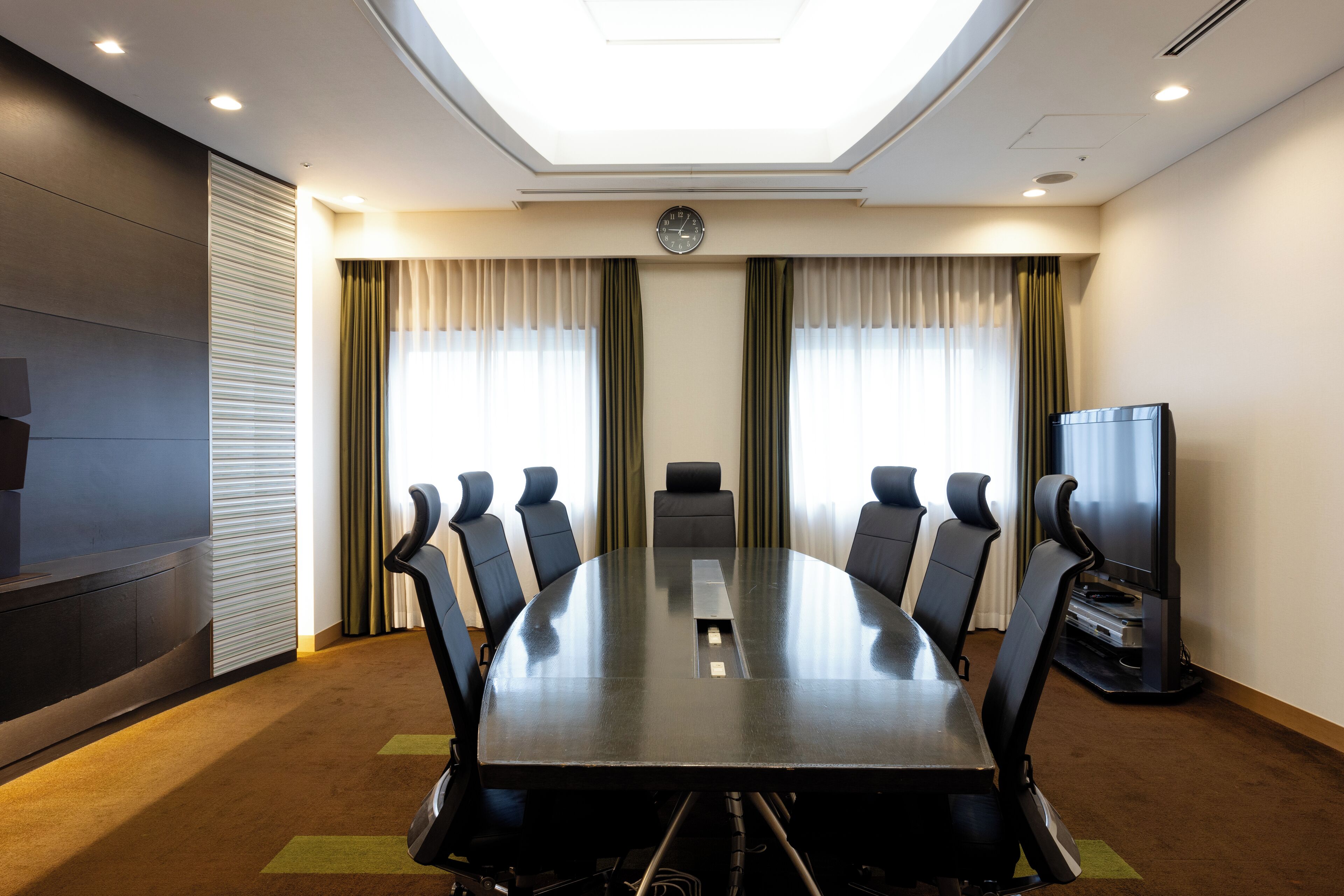 A conference room with a large table, chairs, a clock, and a television.