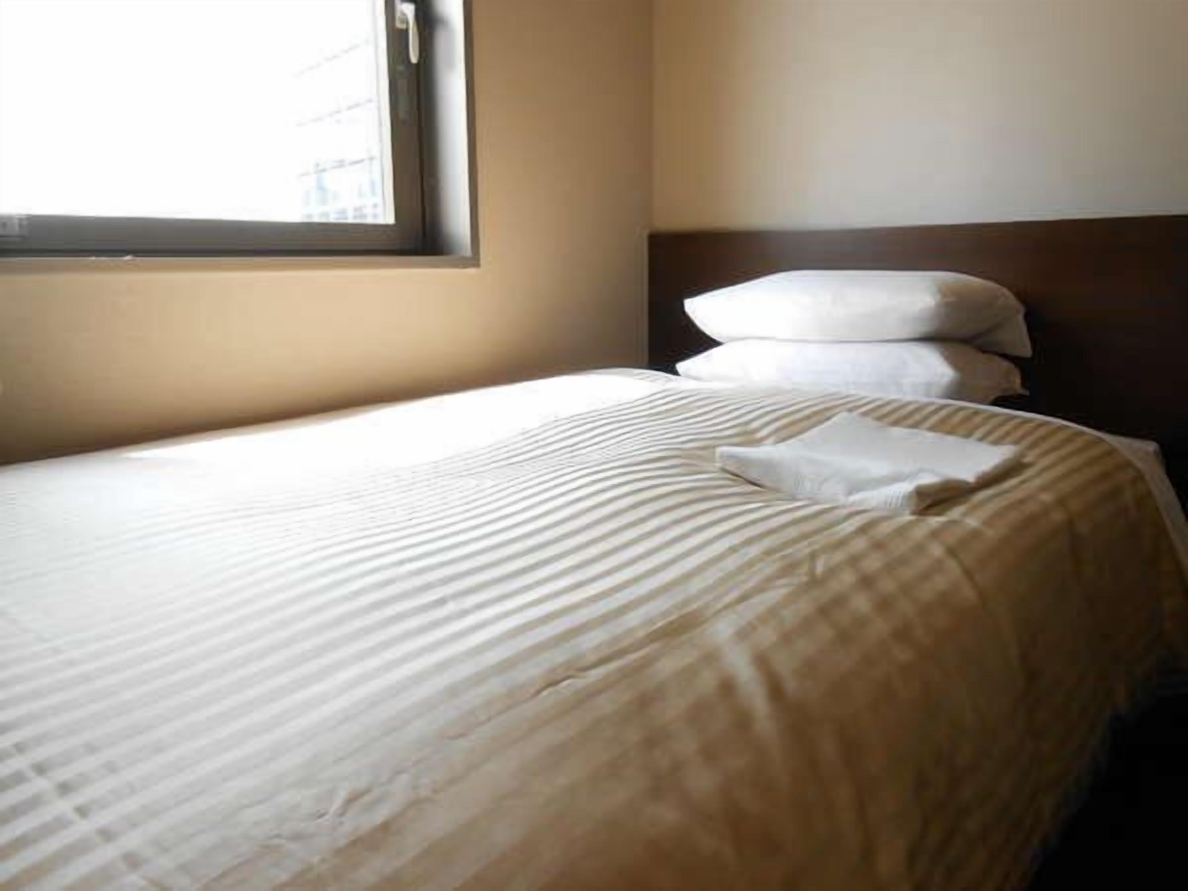 Una habitación de hotel con cama, almohadas y ventana.