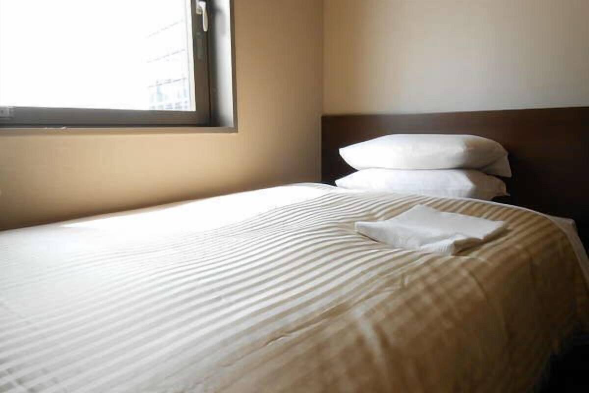 A hotel room with a bed, pillows, and a window.