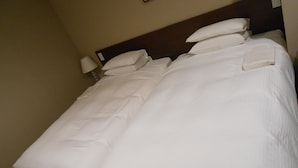 A neatly made bed with white linens and pillows, a wooden headboard, and a bedside lamp. - Hotel Crown Hills Sendai Aobadori (Sendai)