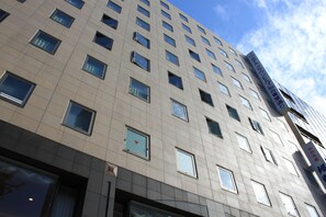Un immeuble à étages doté d’une architecture moderne, caractérisé par une façade à motifs géométriques de fenêtres et une enseigne bien visible sur le côté.