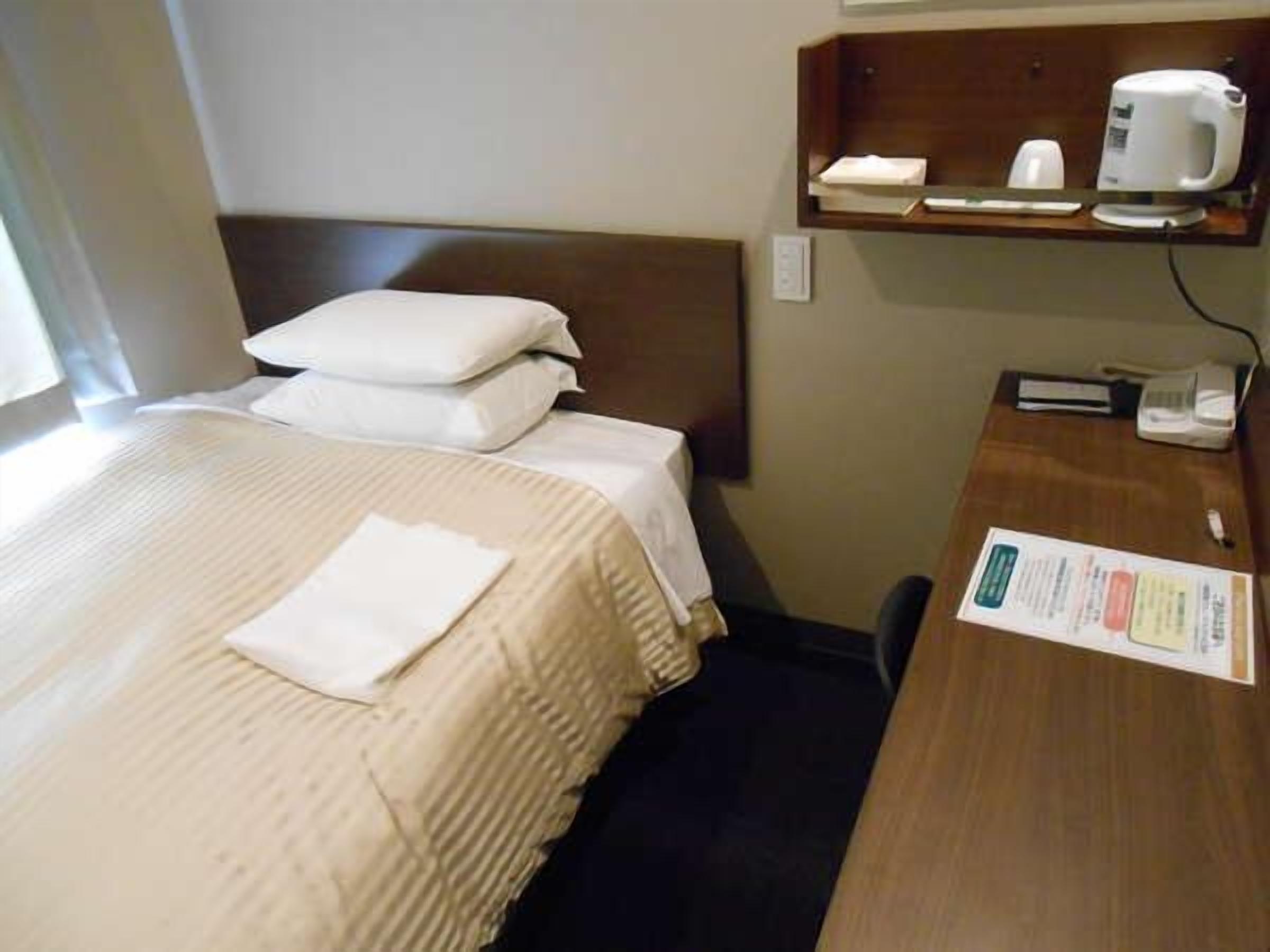 Una habitación de hotel con cama, almohadas, un escritorio con teléfono, cafetera y un menú en la pared.