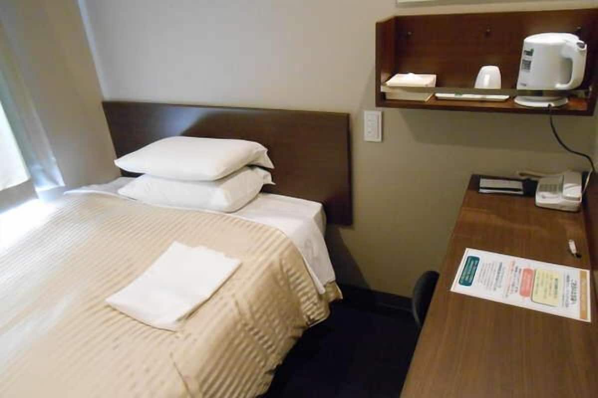 A hotel room with a bed, pillows, a desk with a telephone, a coffee maker, and a menu on the wall.