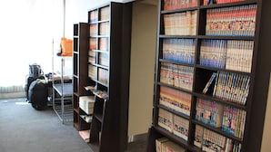 A library with bookshelves filled with books and magazines. There is a luggage cart and a suitcase in the foreground. - Hotel Crown Hills Sendai Aobadori (Sendai)