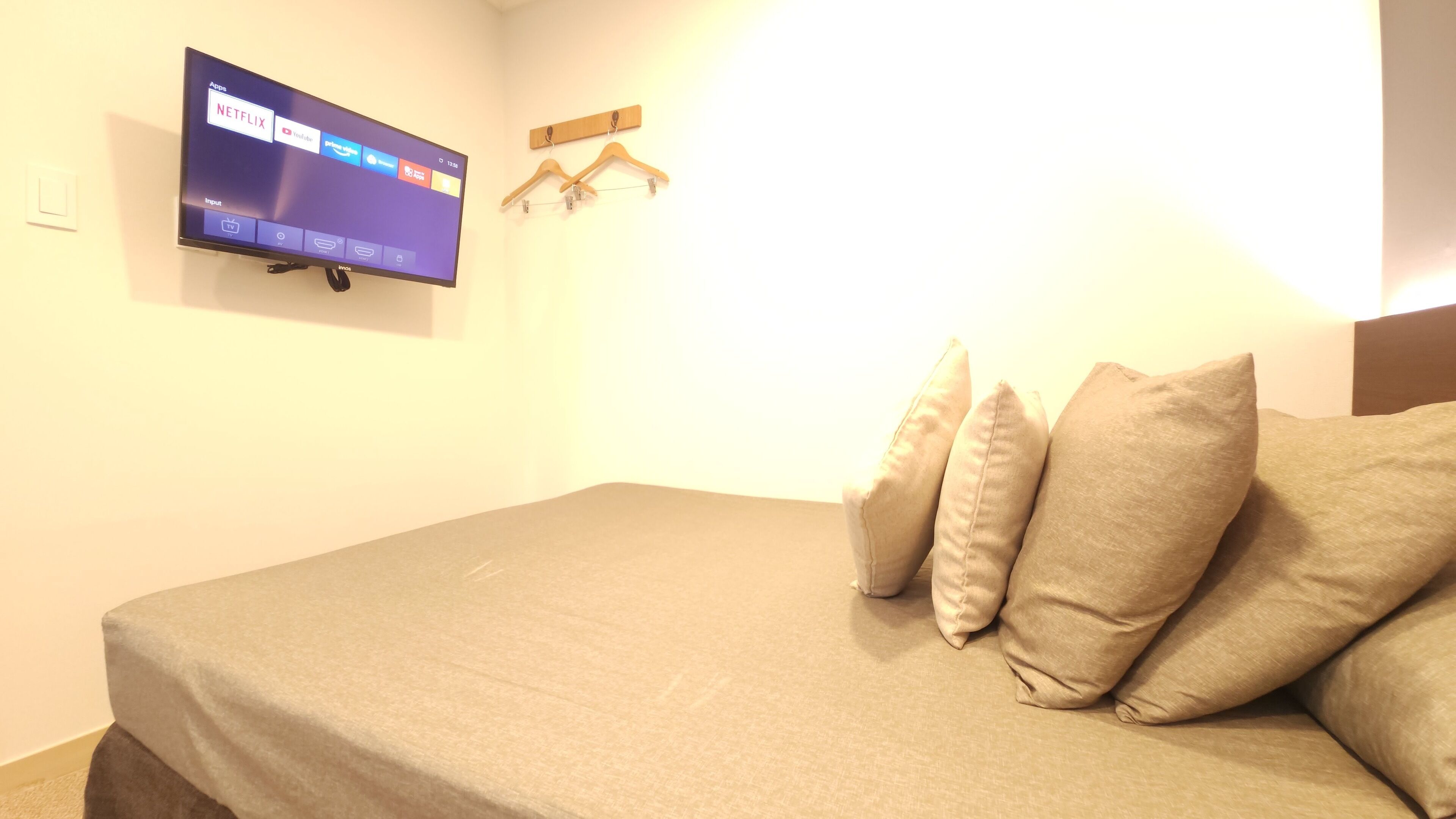 A bedroom with a bed, a TV mounted on the wall displaying app icons, and a wooden hanger on the wall.