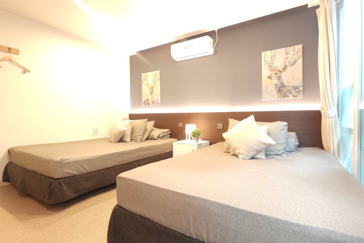 A hotel room with two beds, a nightstand with a lamp and a small plant, and artwork on the walls.