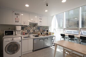 Una cocina moderna con lavadora, microondas y lavabo. Hay carteles en la pared y una ventana con vistas a la ciudad.