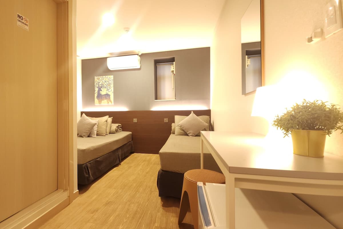 A small, well-lit room with two beds, a desk, and a potted plant.