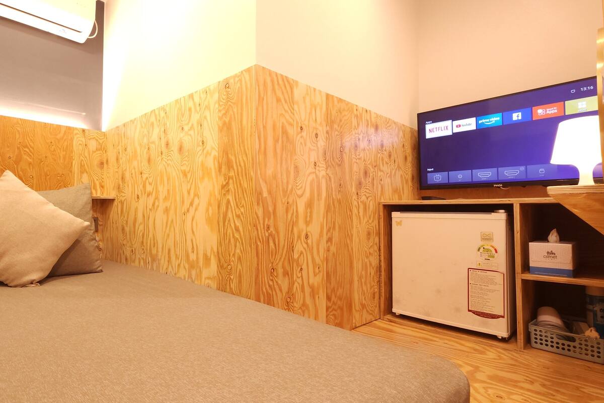 A hotel room with a bed, a television, a small refrigerator, and a wooden wall.