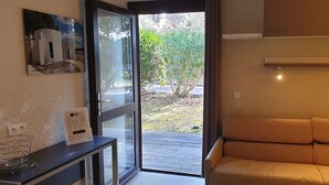 A modern room with a glass door leading to an outdoor area, a sofa, a small table with a power outlet, and a framed picture on the wall. - Belambra Clubs La Colle-sur-Loup - Les Terrasses De Saint-Paul De Vence (La Colle-sur-Loup)