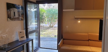Una habitación moderna con puerta de vidrio que da a un espacio exterior, un sofá, una mesita con toma de corriente e imagen enmarcada en la pared.