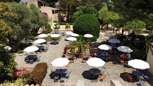 An outdoor patio with multiple tables and umbrellas, surrounded by greenery and trees. - Belambra Clubs La Colle-sur-Loup - Les Terrasses De Saint-Paul De Vence (La Colle-sur-Loup)