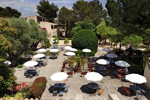 Un patio al aire libre con varias mesas y sombrillas, rodeado de follaje y árboles.