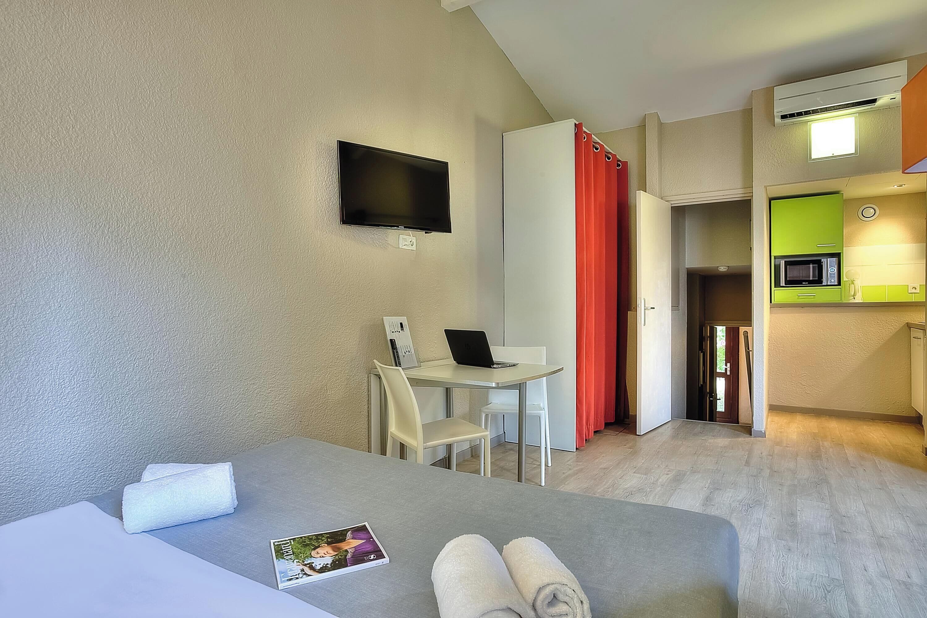 Une chambre d’hôtel équipée d’un lit, d’un bureau, d’une chaise, d’un téléviseur à écran plat, d’un four à micro-ondes et d’une kitchenette.
