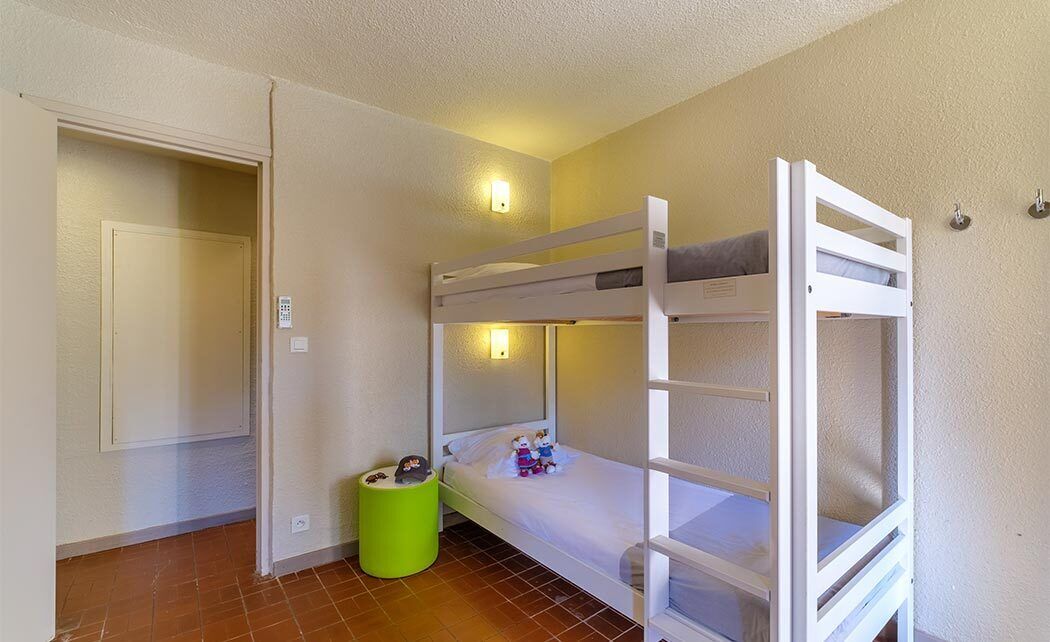 A bunk bed room with a green trash bin, a door, and a wall-mounted light fixture.