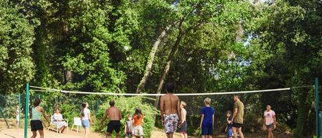 Een groep mensen speelt volleybal in een open omgeving, met bomen op de achtergrond.