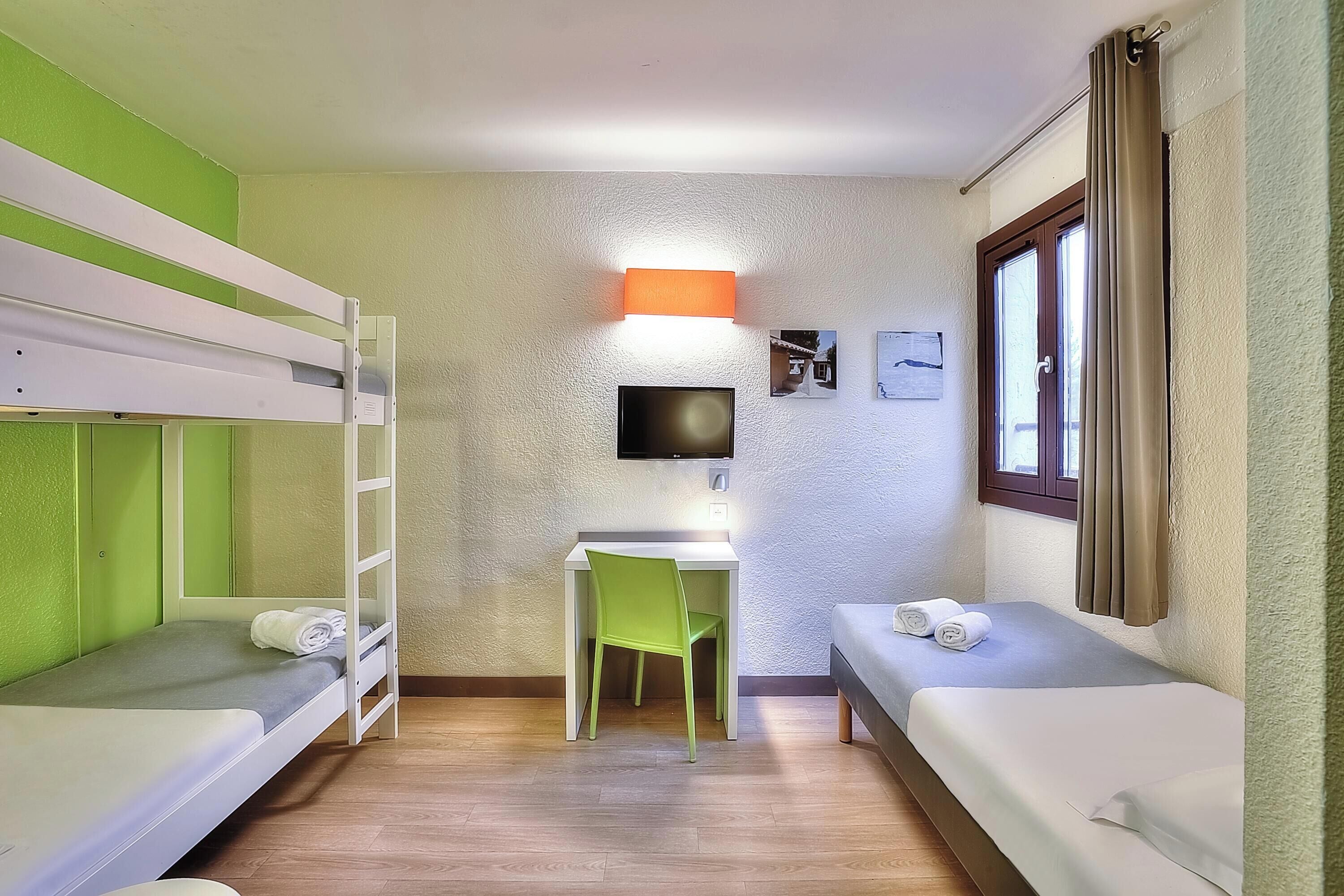 A small, well-lit room with bunk beds, a desk, and a chair.