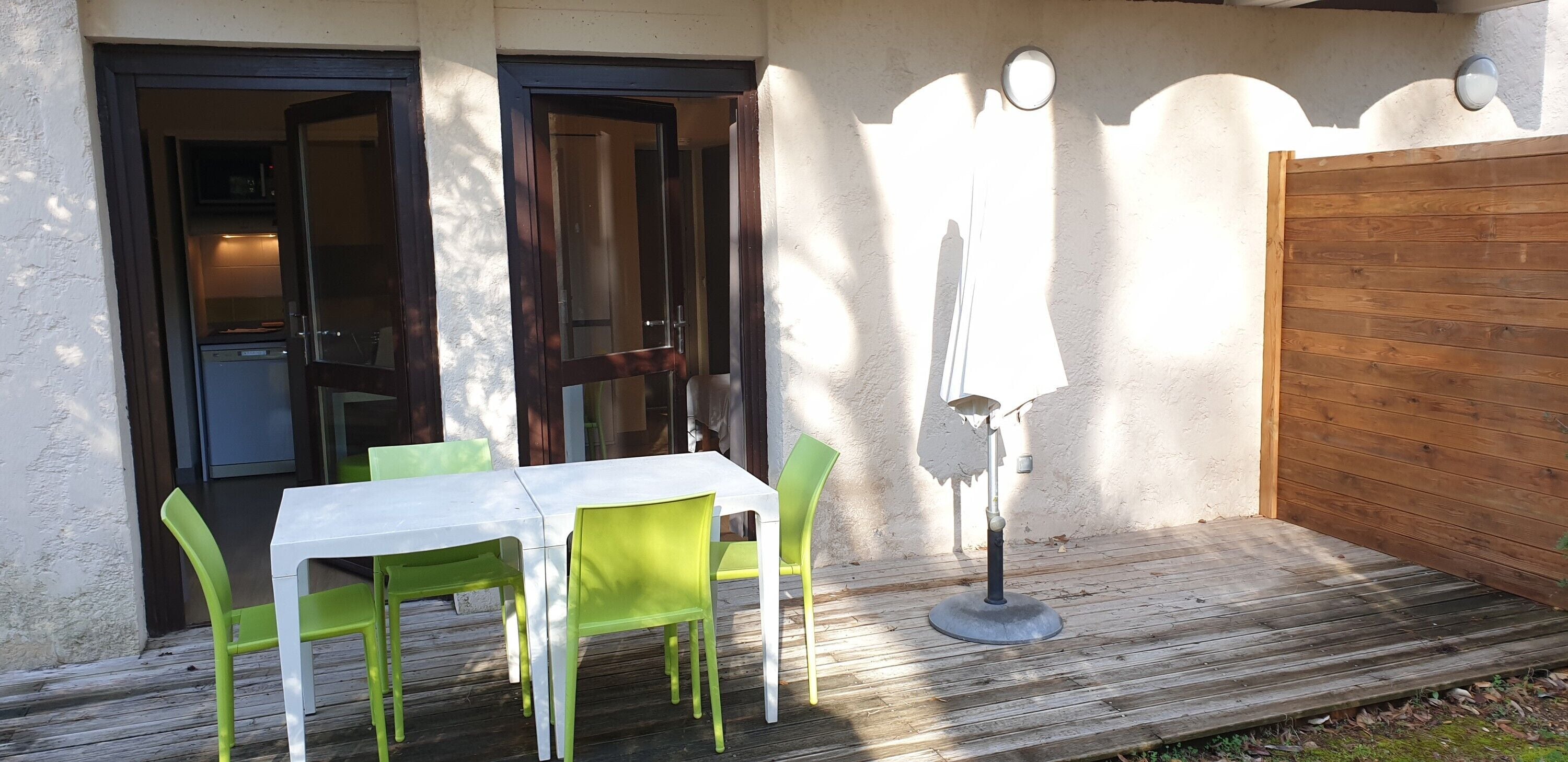 A patio with a white table and green chairs, a wooden deck, and a wooden fence.