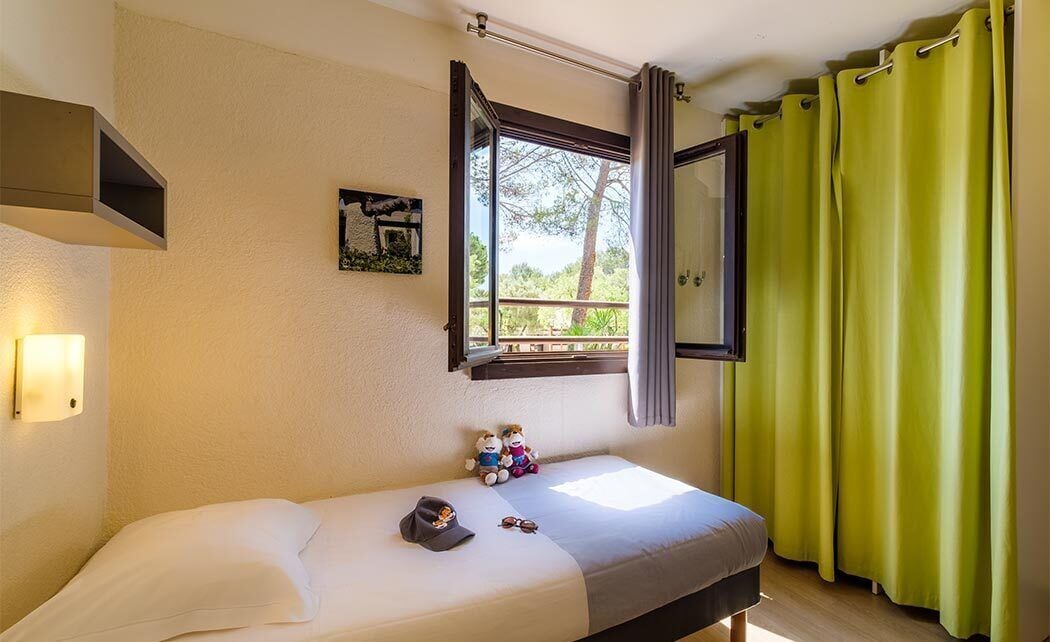 A single bed with a headboard, a window with curtains, a wall-mounted shelf, and a small wall decoration.