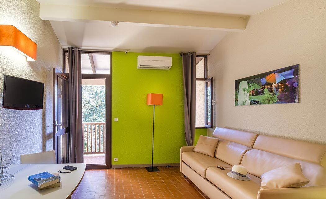 A room with a green wall, a beige sofa, a flat-screen TV, a table with books, and a painting.