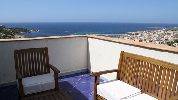 A balcony with two wooden chairs and a view of the sea and a town. - M'ama Holiday Rooms (Palermo)