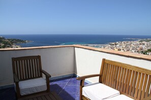 A balcony with two wooden chairs and a view of the sea and a town. - M'ama Holiday Rooms (Palermo)