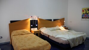 A hotel room with two beds, a wooden headboard, bedside lamps, and a wall-mounted light fixture. - M'ama Holiday Rooms (Palermo)