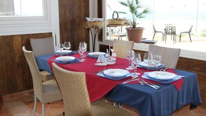A dining table set with plates, glasses, and cutlery, surrounded by wicker chairs, with a view of the outdoors. - M'ama Holiday Rooms (Palermo)
