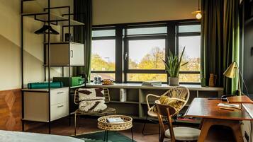 Une chambre à coucher moderne, équipée d’un lit, d’un bureau, d’une chaise, d’une bibliothèque et d’une fenêtre donnant sur des arbres.