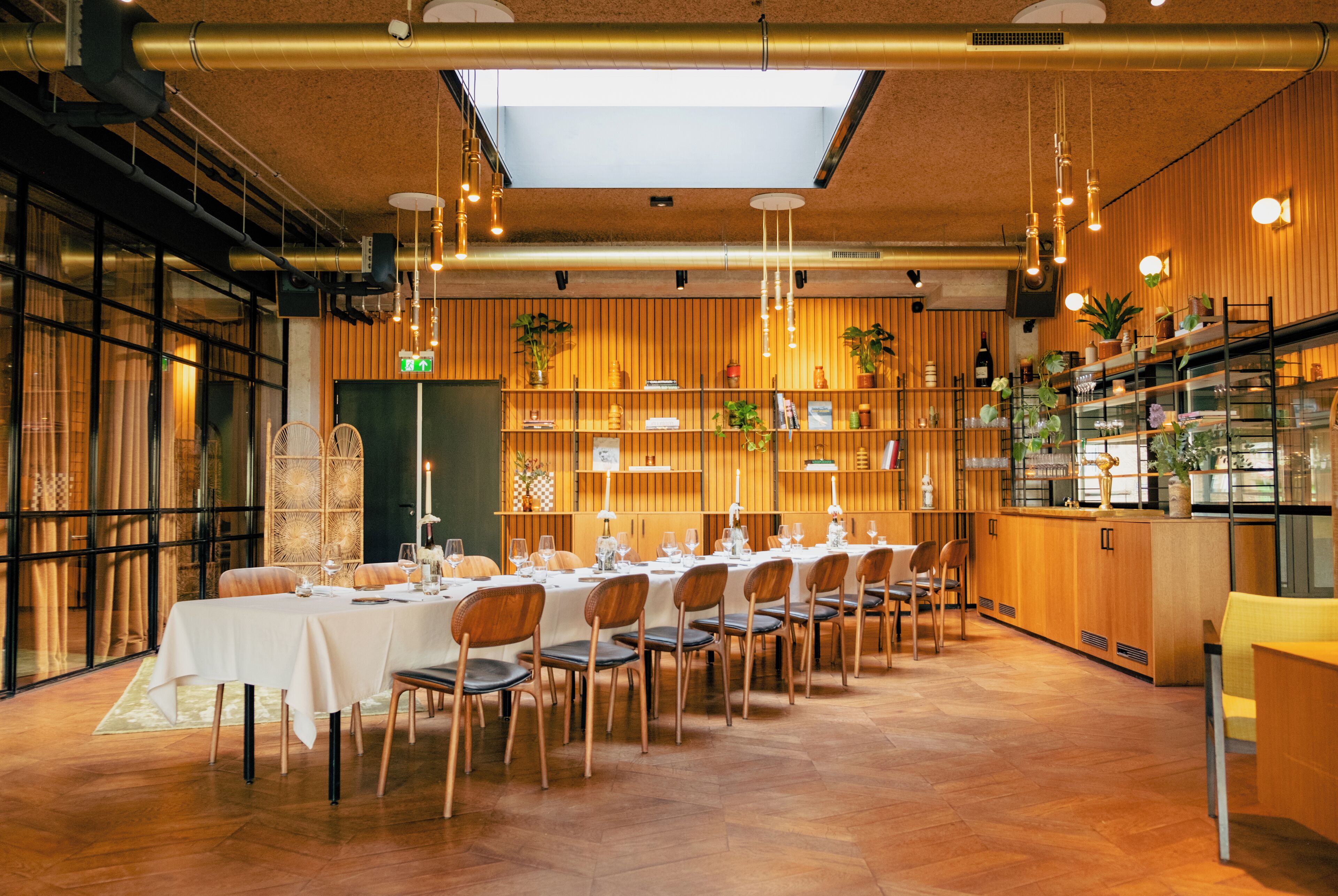 A restaurant with a long dining table set for a meal, wooden walls, and hanging lights.