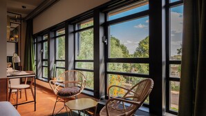 Una habitación con ventanas amplias, sillas de mimbre, una mesita y un escritorio con una lámpara.