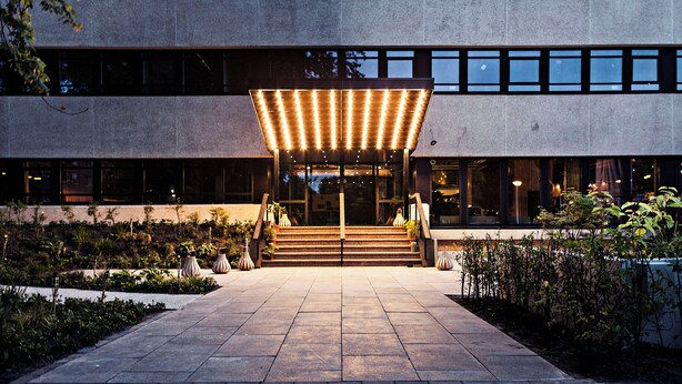 Entrada de un edificio moderno con un vestíbulo cubierto, escalones y un jardín.