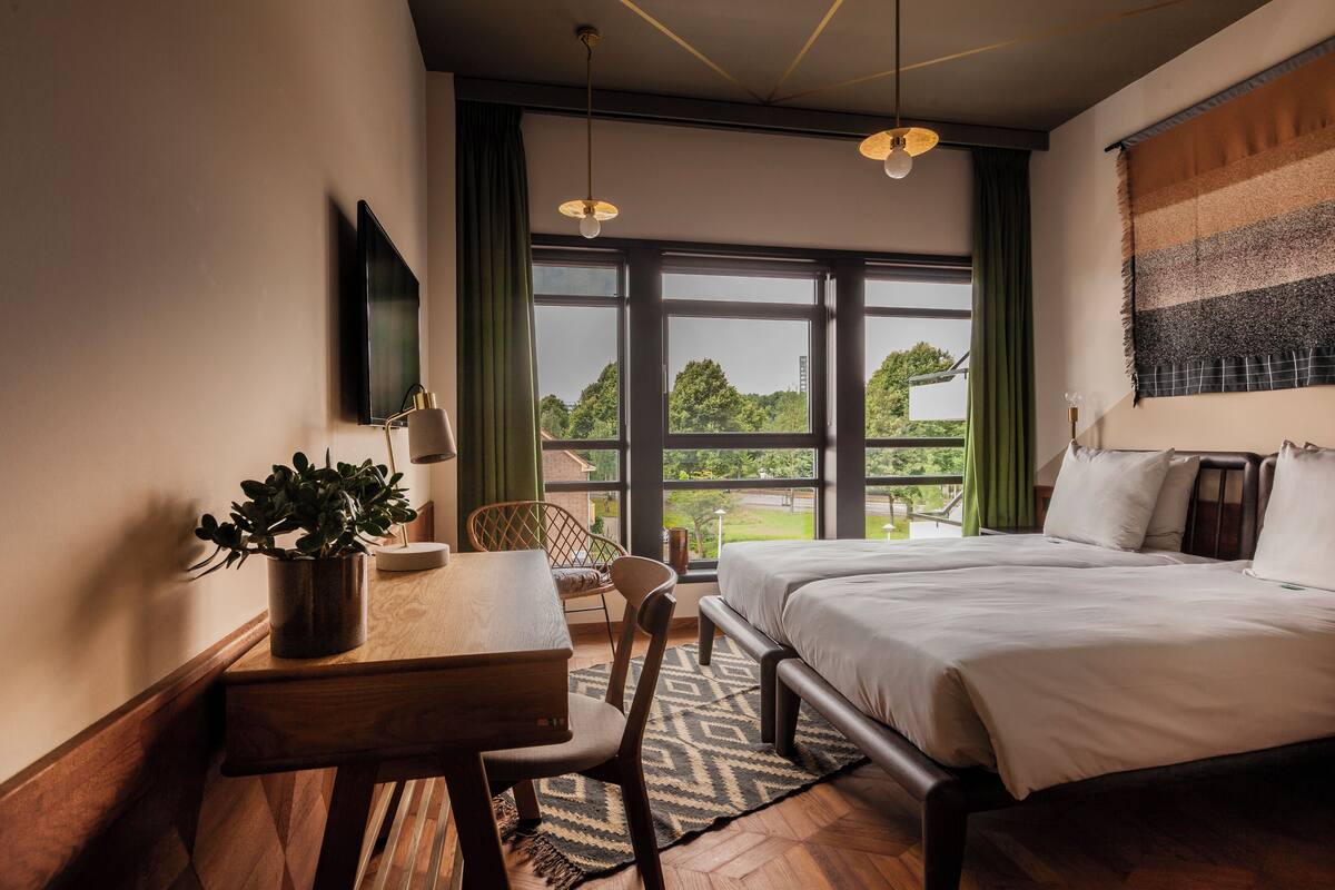 Une chambre d’hôtel équipée d’un lit, d’un bureau, d’une chaise, d’une télévision et d’une fenêtre donnant sur l’extérieur.