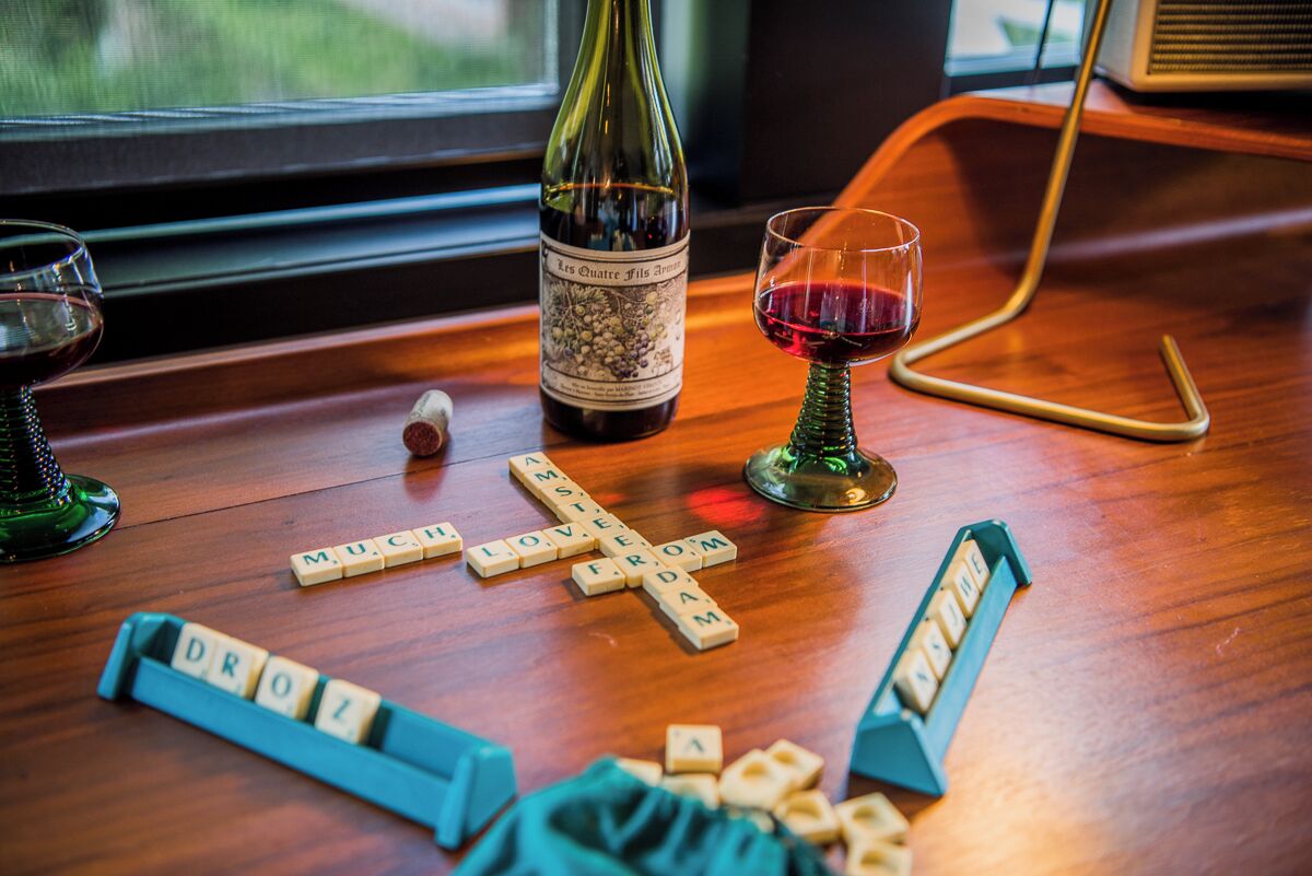 Une table en bois, une bouteille de vin, un verre de vin rouge et un jeu de Scrabble.