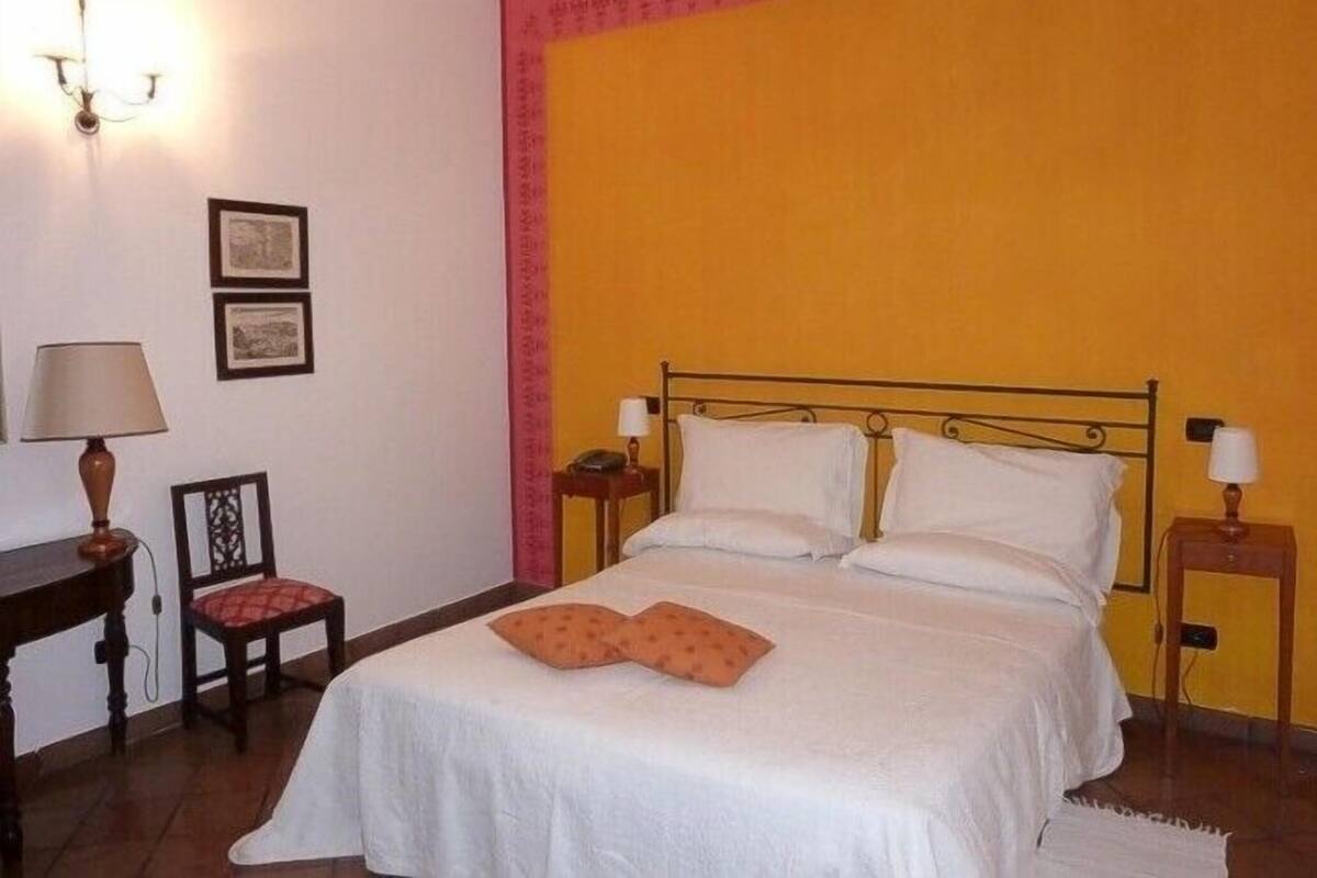 Un dormitorio con una cama, dos mesitas de noche, una silla y dos lámparas de pared.