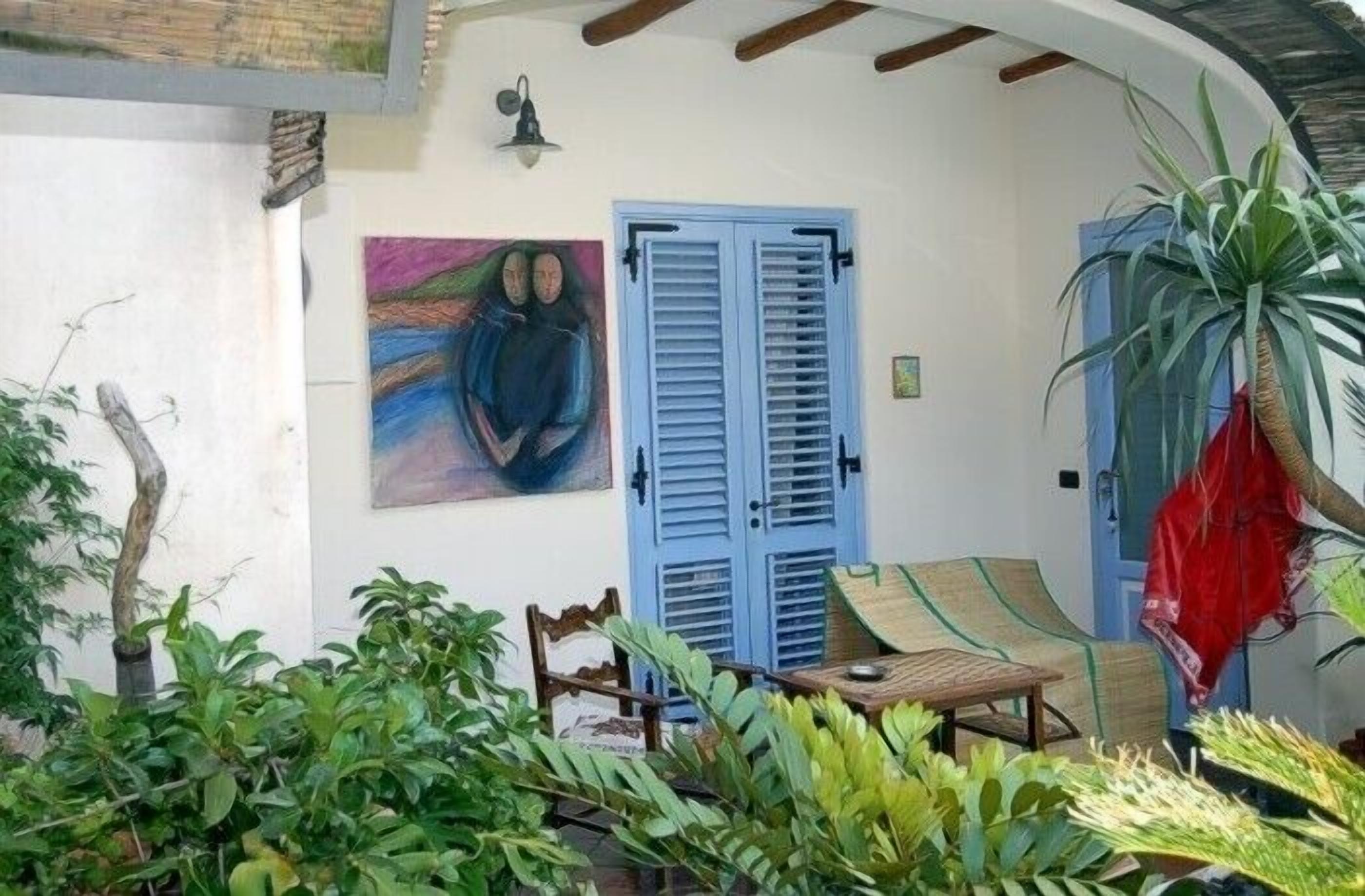 Un espace extérieur accueillant avec une table et des chaises en bois, une porte à volets bleus et un tableau accroché au mur.