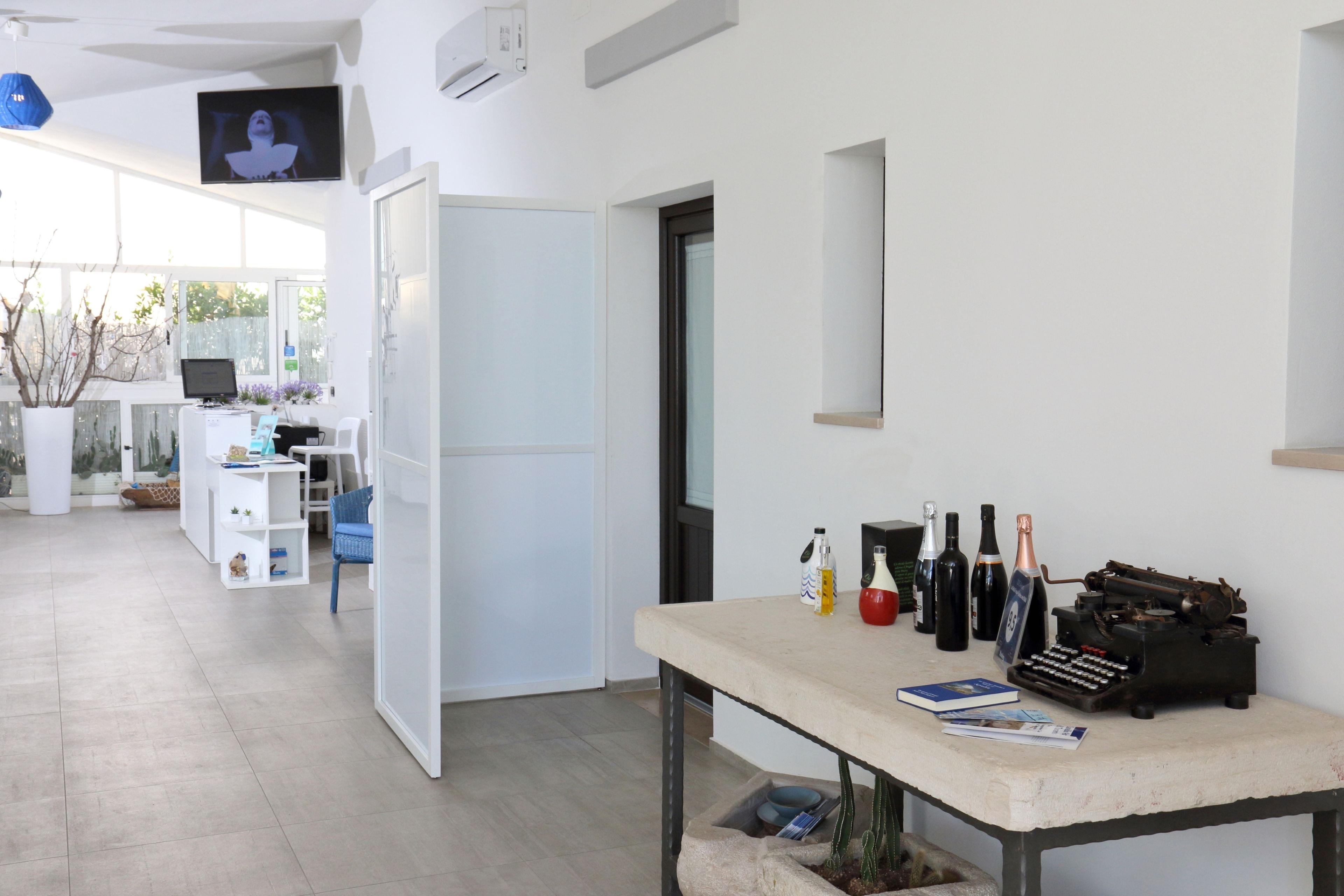 Un espacio de oficina moderno con un escritorio, computadora y varios objetos, incluyendo botellas y una máquina de escribir.