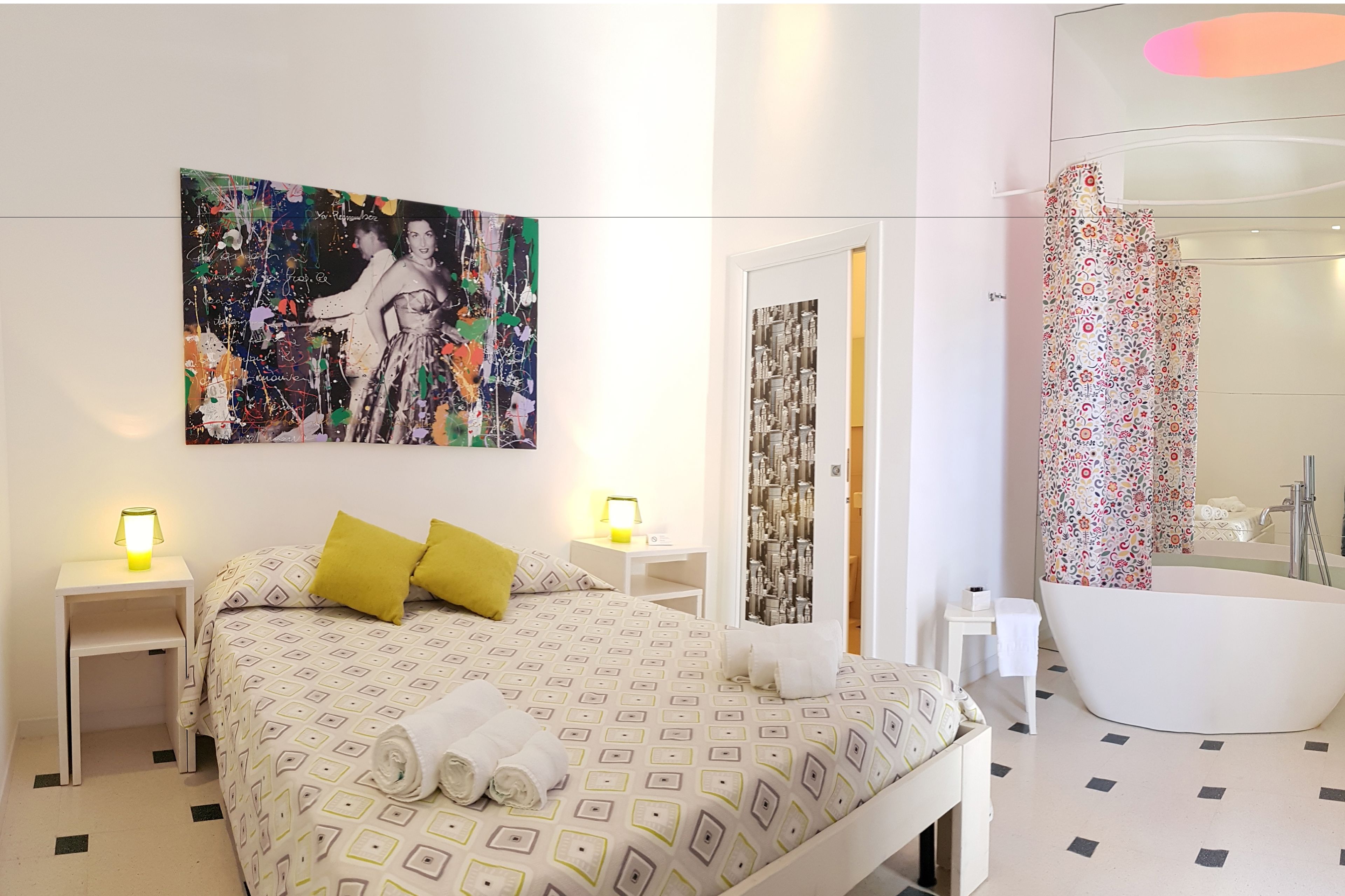 Una habitación de hotel moderna con una cama, un cuadro abstracto grande, un baño con bañera y cortina de ducha.