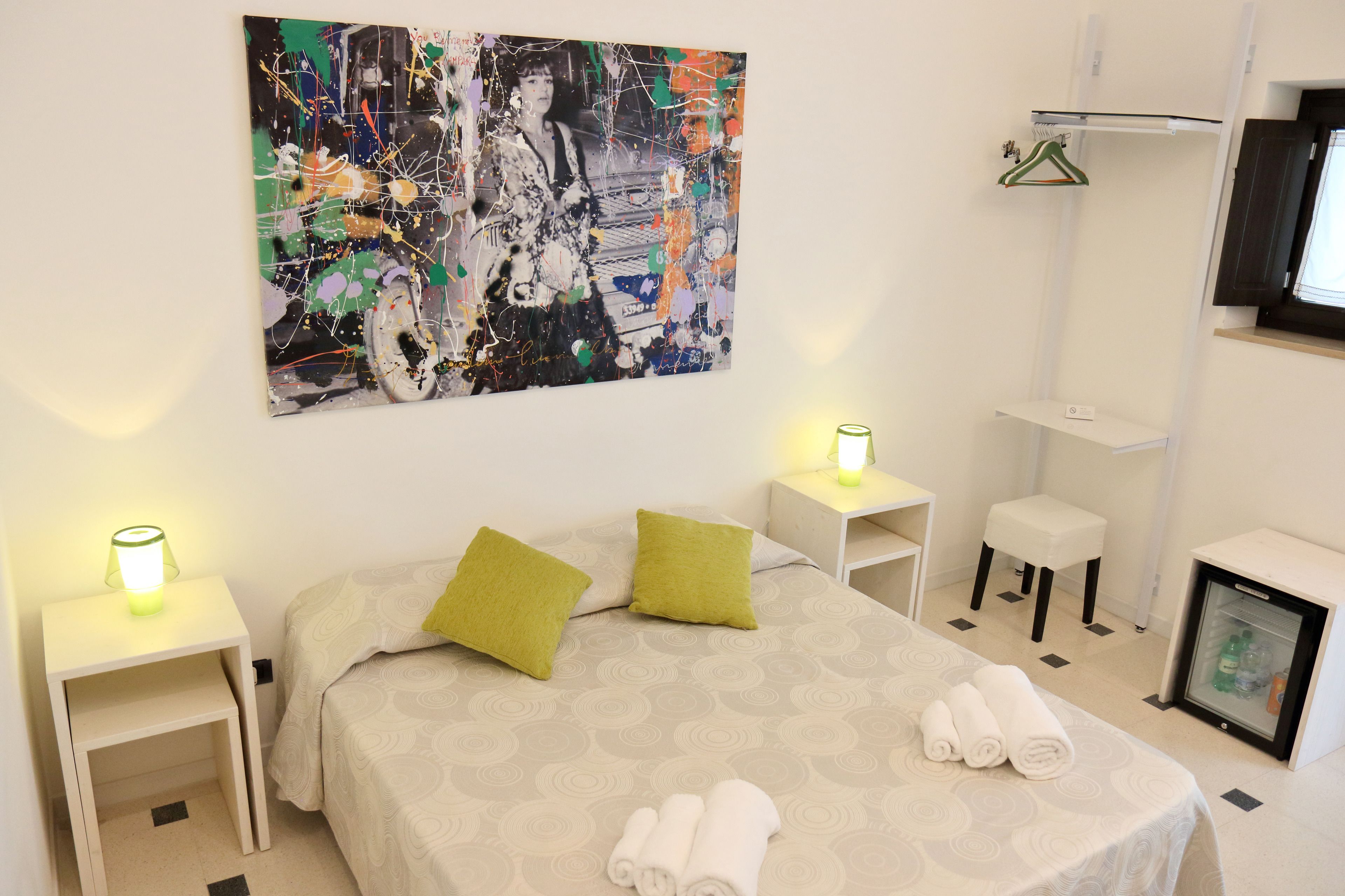 Habitación de hotel con cama, dos mesitas de noche, un pequeño rincón de descanso, televisor montado en la pared y un mini refrigerador.