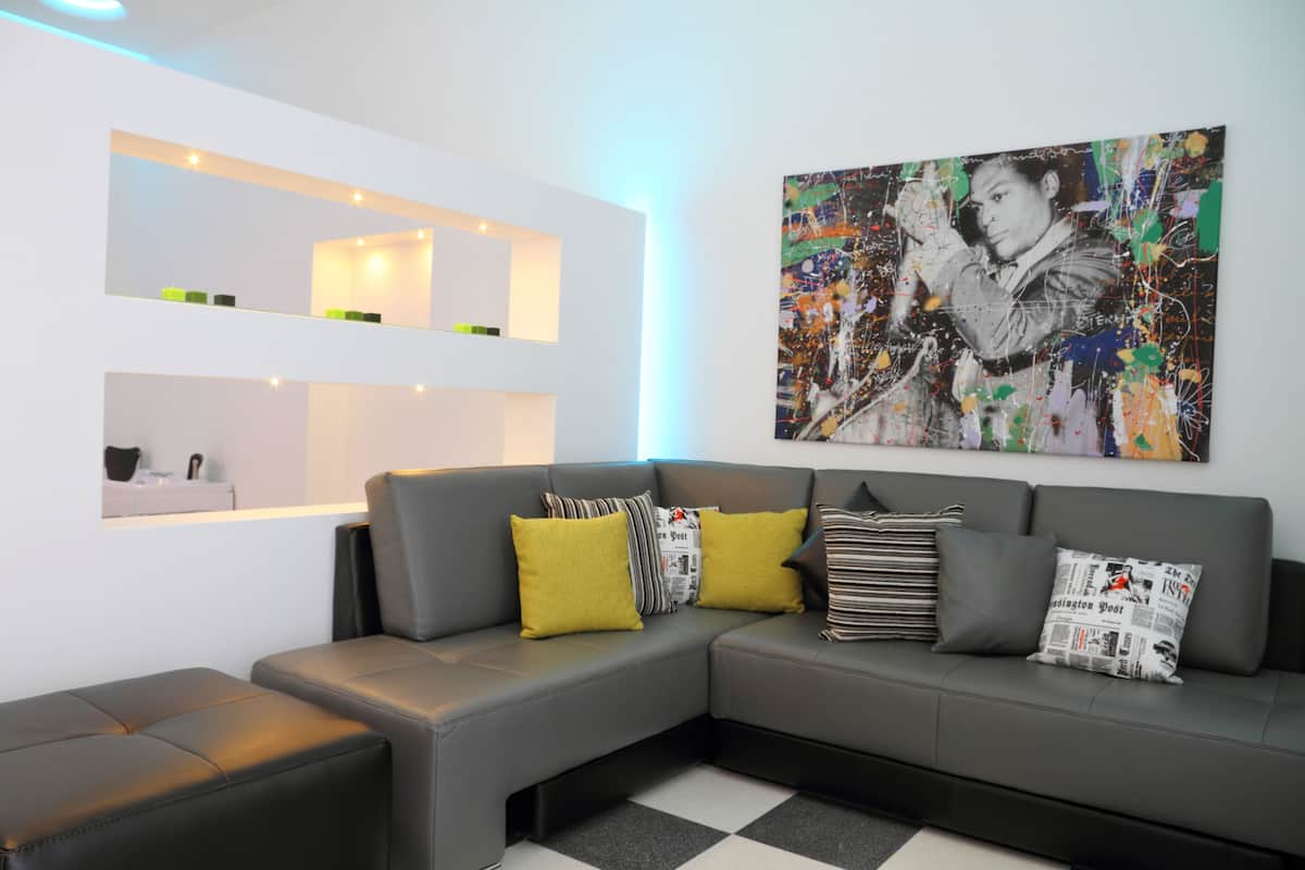 A modern living room with a grey sectional sofa, yellow and striped pillows, and a large abstract painting on the wall.