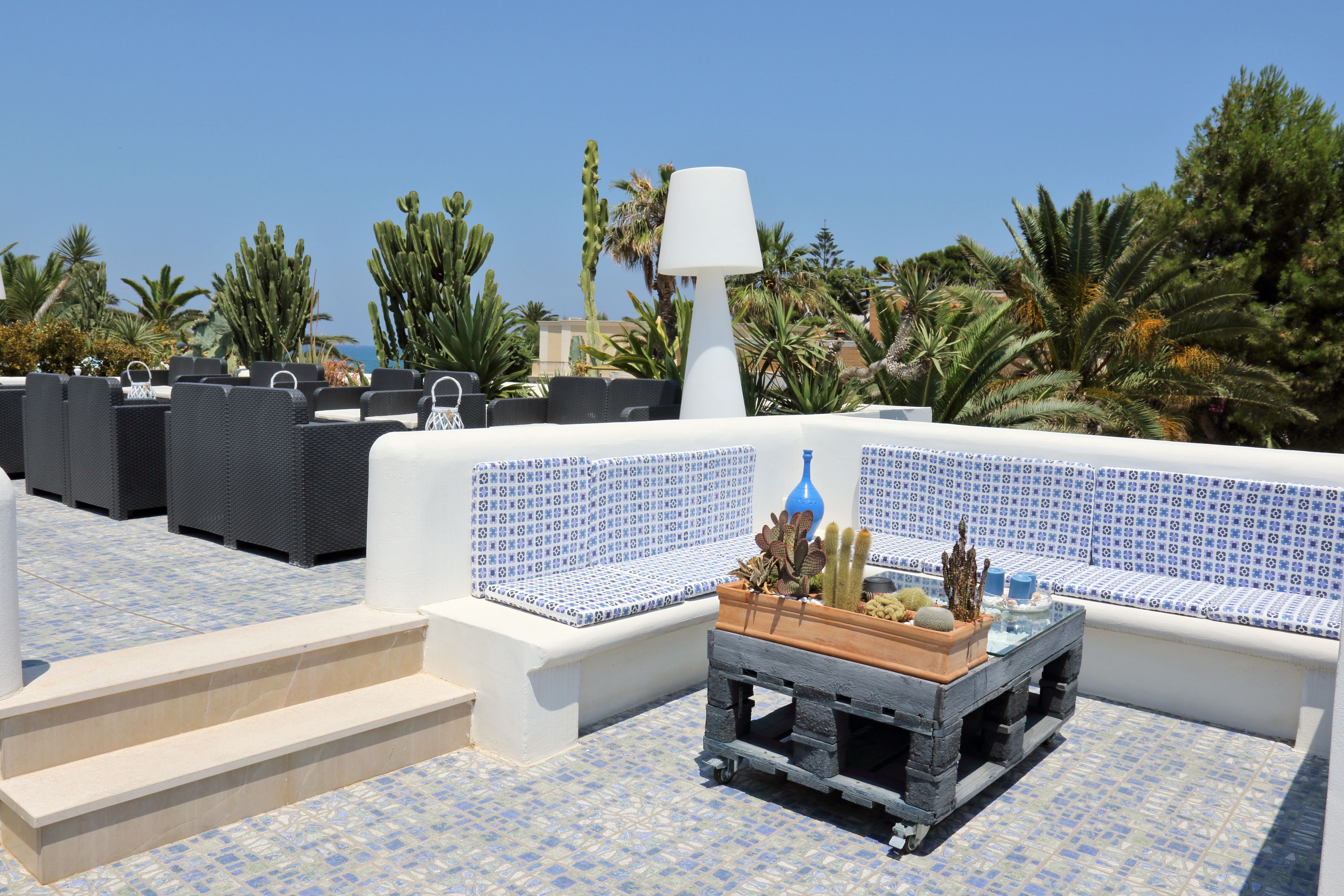 Une terrasse sur le toit, aménagée avec des sièges d’extérieur, une lampe et un jardinier contenant des cactus et des plantes succulentes.