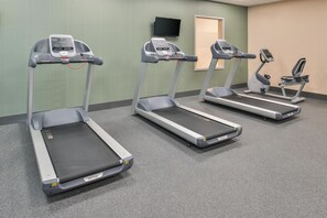 Three treadmills in a room with a green wall and a television mounted above.